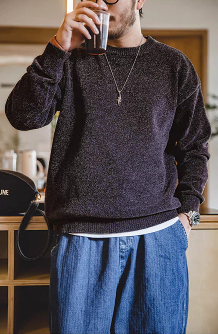 Man wearing dark purple chenille sweater holding a cup of coffee in a casual indoor scene