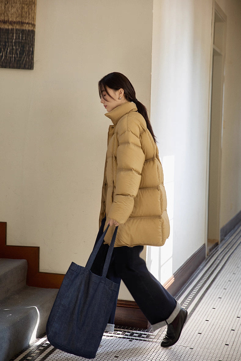 Side view of caramel brown Cloud-Contour Down Coat as woman walks with dark denim tote bag
