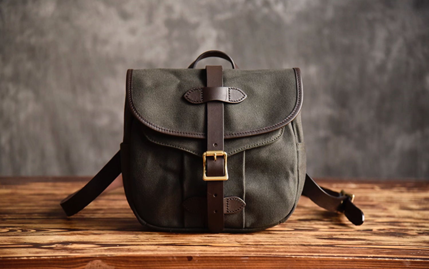 Front view of Olive Green Nomad waxed canvas satchel with leather buckle strap.