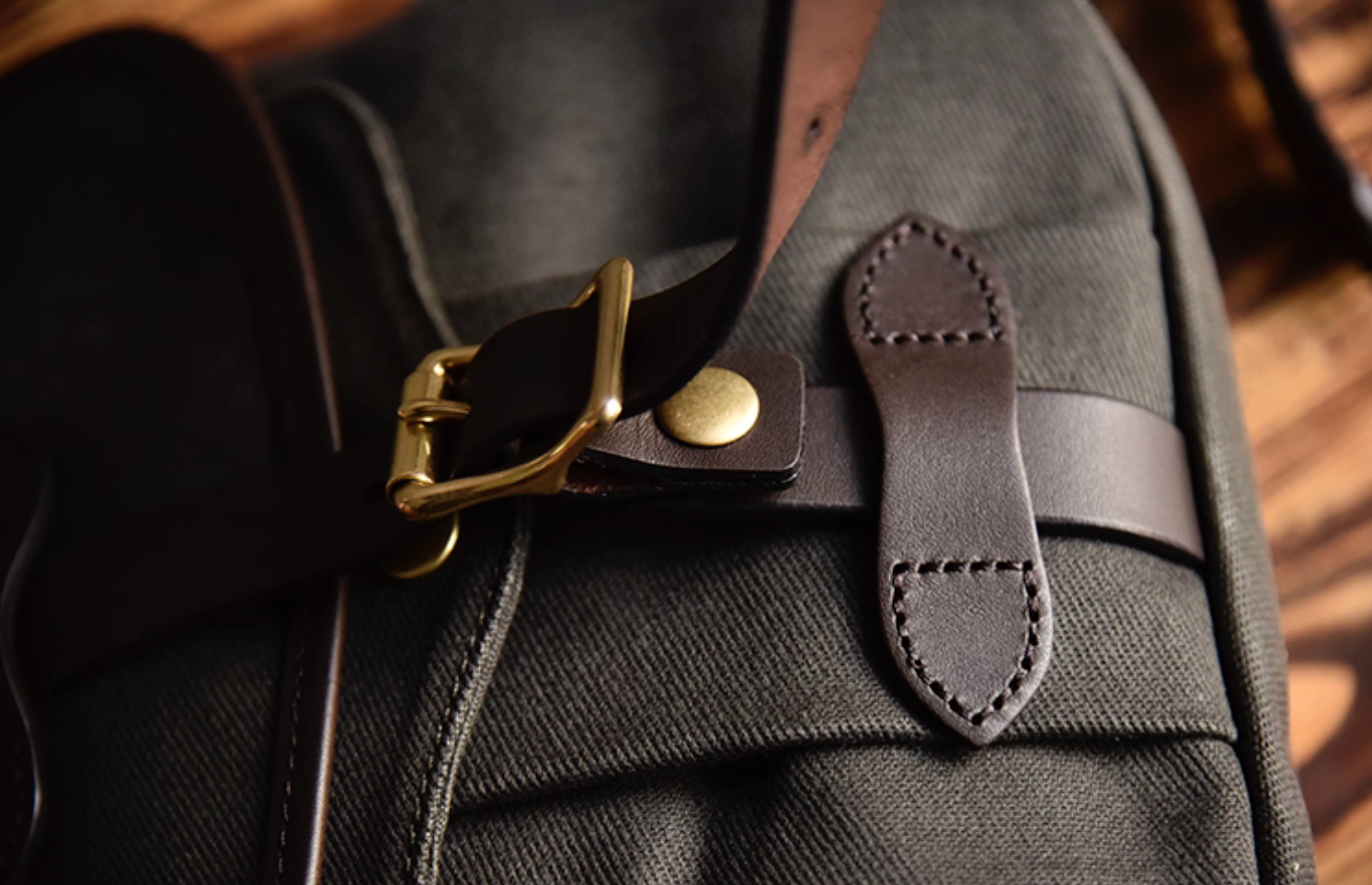 Close-up of Olive Green Nomad satchel showing brass buckle and stitching detail.