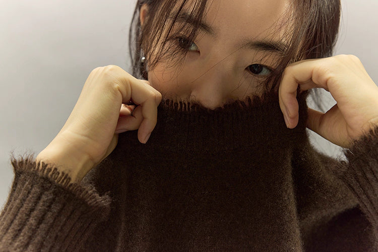 Woman pulling collar of dark coffee yak sweater playfully, showing softness of knit.