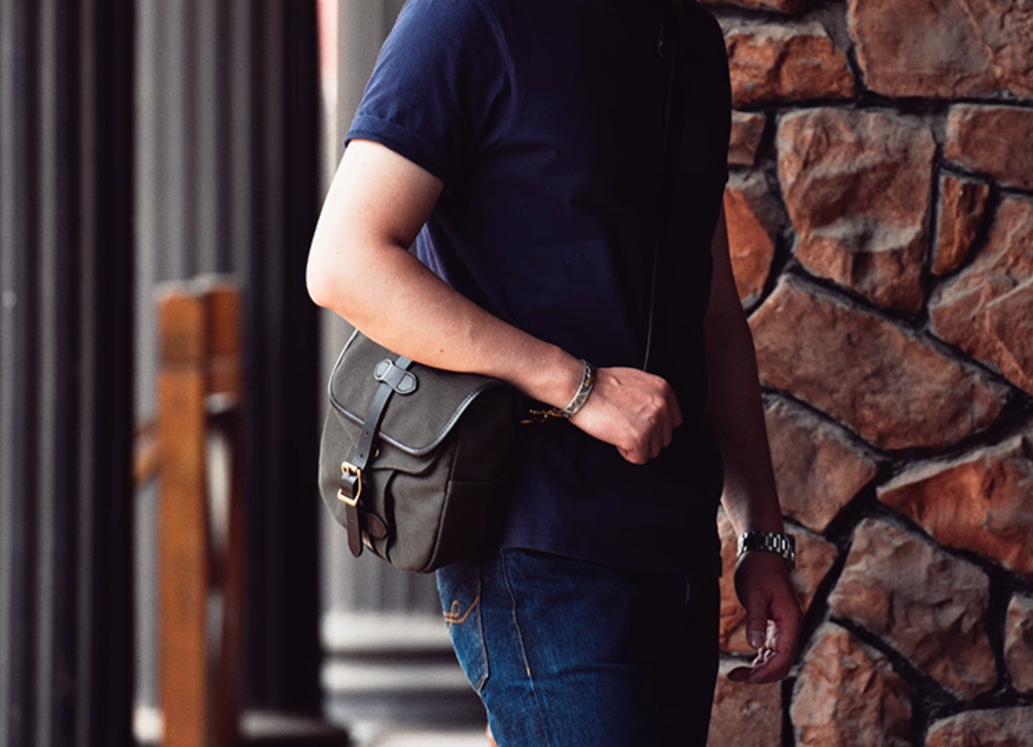 Man wearing Olive Green Nomad satchel crossbody with jeans and navy shirt.