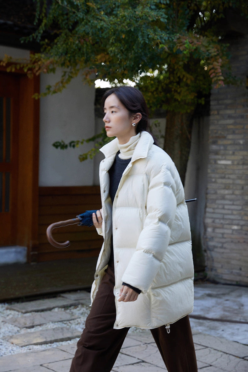 Outdoor side view of off white Cloud-Contour Down Coat as woman walks holding an umbrella