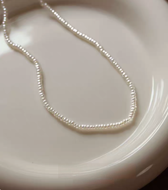 Classic pearl silver necklace single strand flat lay on ceramic plate featuring fine small freshwater pearls on delicate silver chain