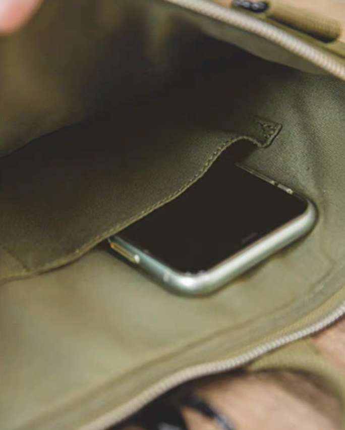 Close-up of the interior of the army green canvas tote bag showing a smartphone stored in an internal pocket.