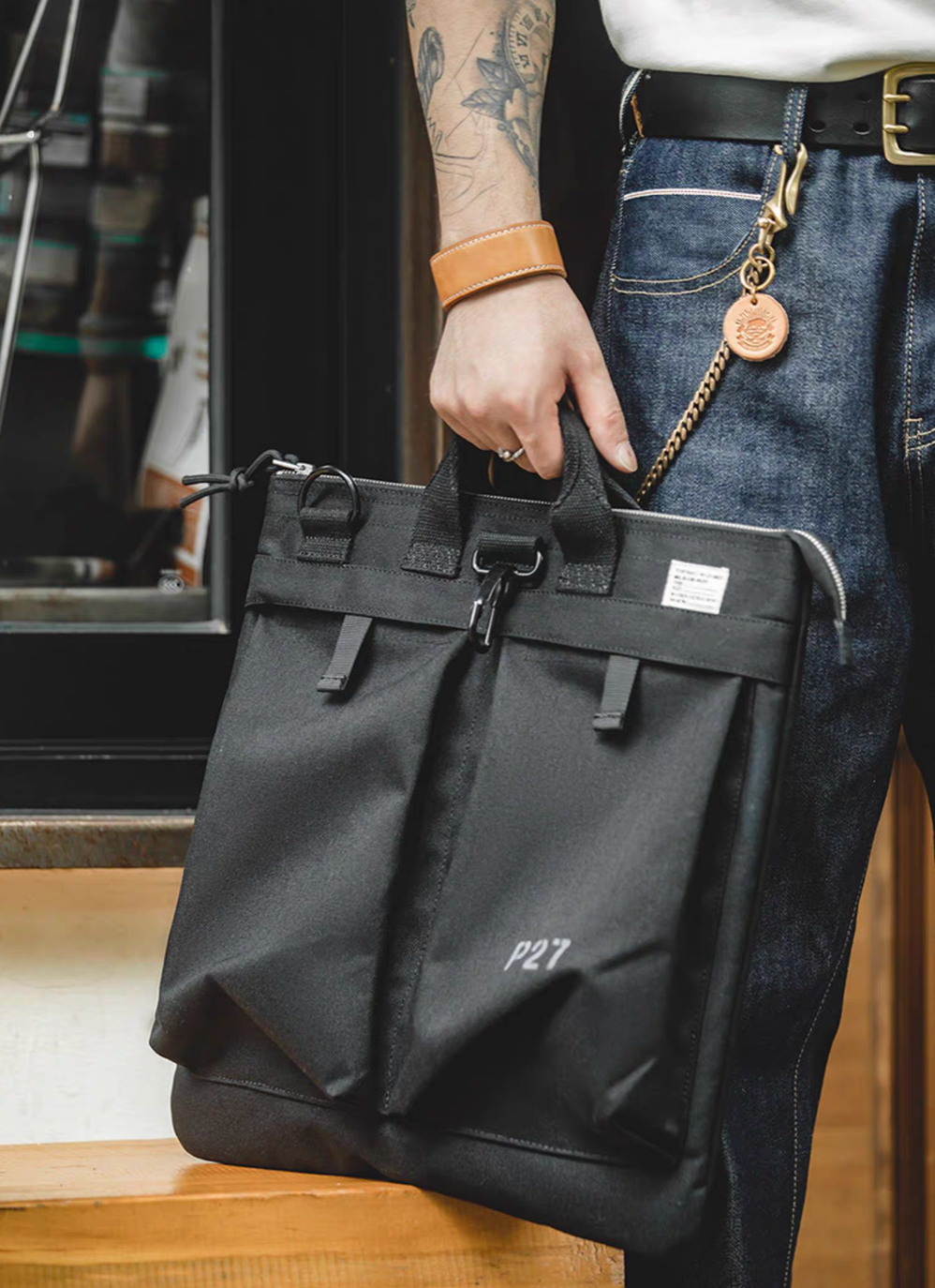 Person holding charcoal black canvas tote bag by top handles, showcasing everyday carry style and front pocket structure.