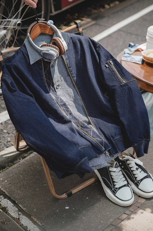 Denim MA-1 bomber jacket draped on chair with shirt and sneakers beside it