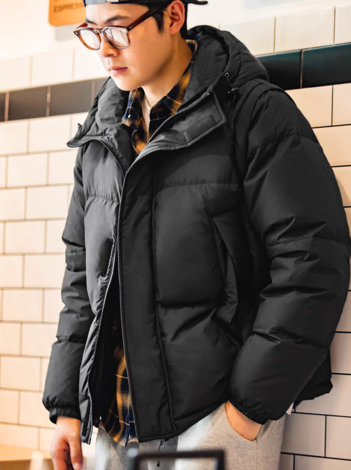 Side view of model in black parka indoors showing hood and zipper detail
