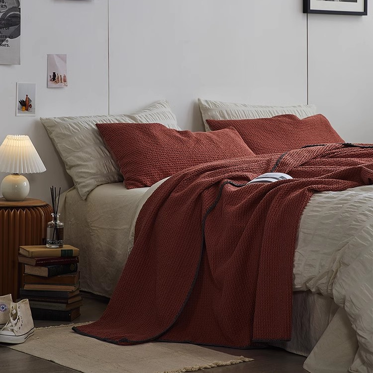 Burgundy waffle honeycomb cotton throw blanket elegantly draped across a bed creating a cozy layered bedding look.