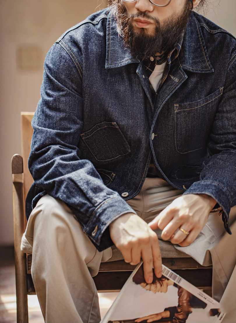 Model seated wearing denim chore coat with heritage-style design