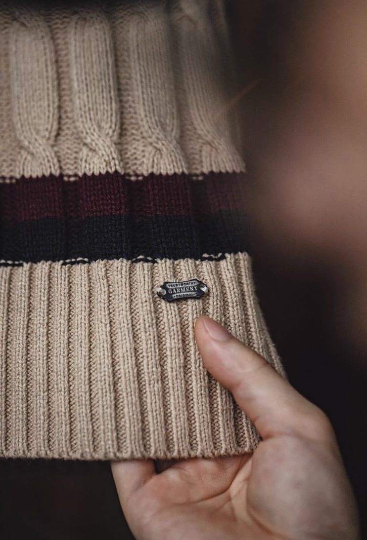 Close-up of ribbed hem and metal logo plate on khaki knit vest