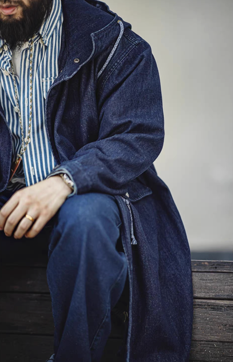 Man sitting casually wearing long denim fishtail parka with striped shirt