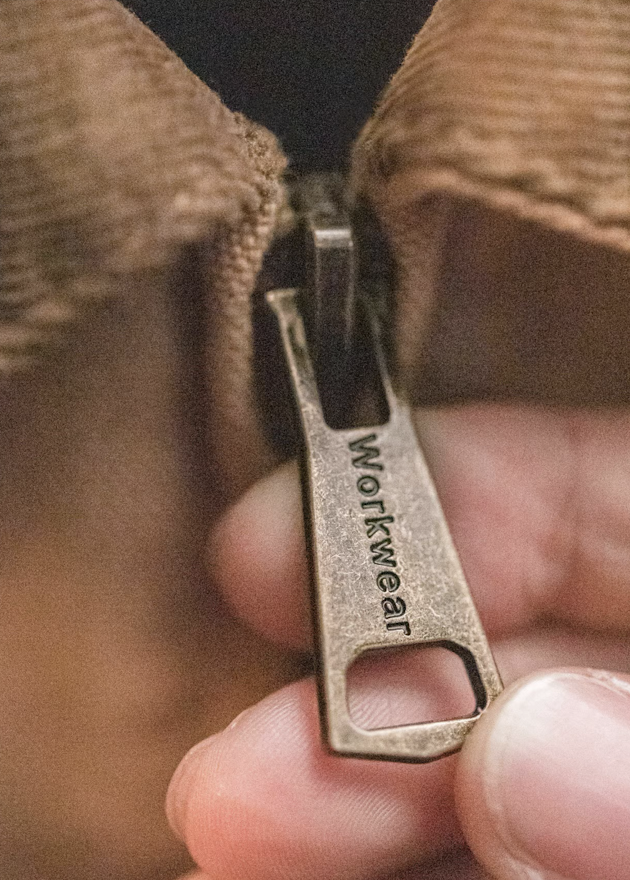 Close-up of brass zipper pull engraved with Workwear text on khaki Santafe jacket.