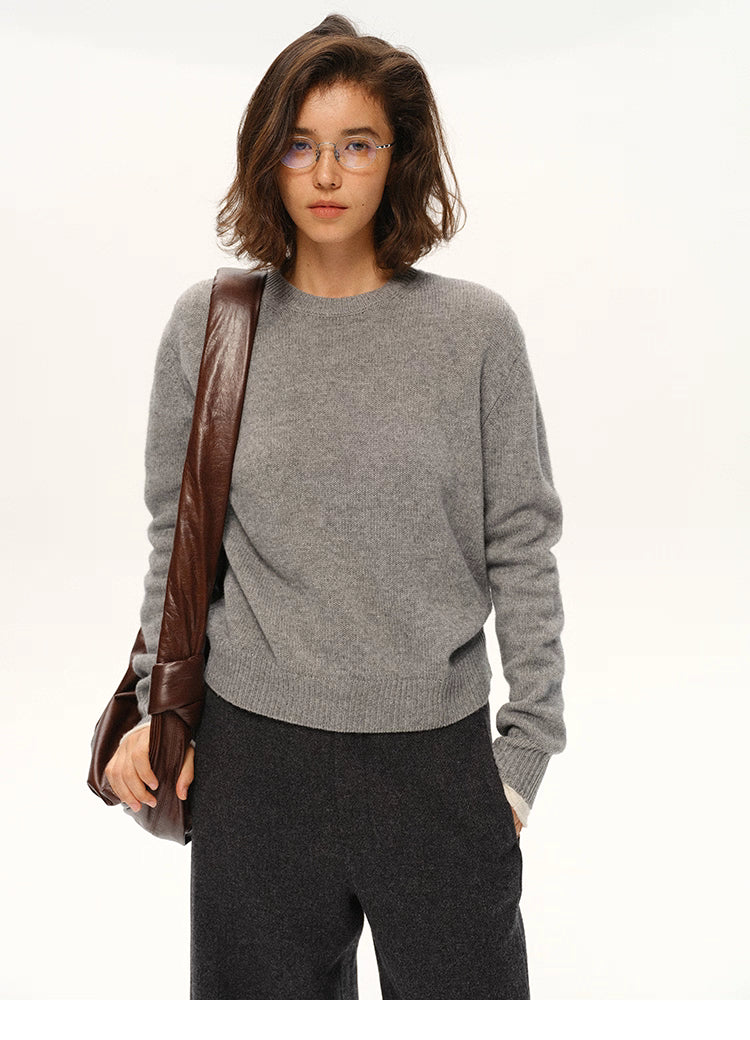 Woman in medium gray cashmere-blend crewneck sweater holding brown leather shoulder bag.