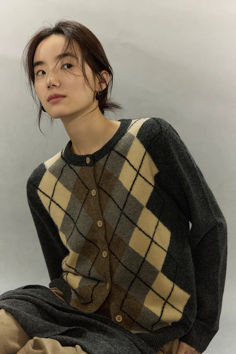 Model wearing dark gray argyle wool blend cardigan sitting calmly against neutral background