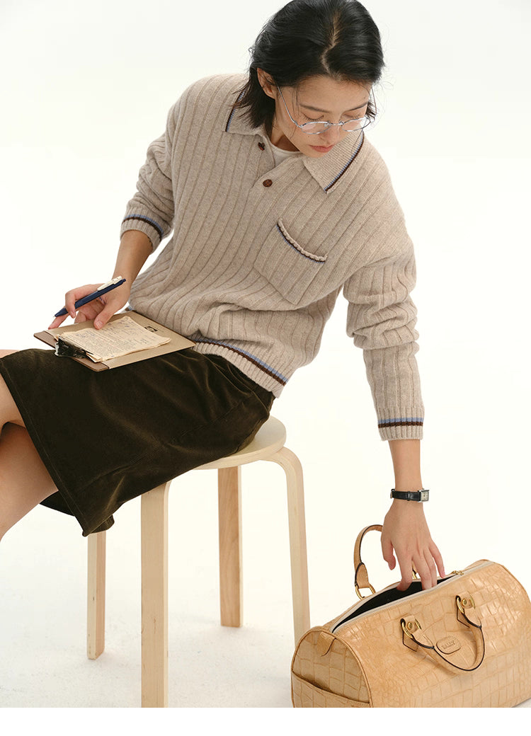Model seated while writing, wearing the ribbed wool polo sweater with contrast trim.