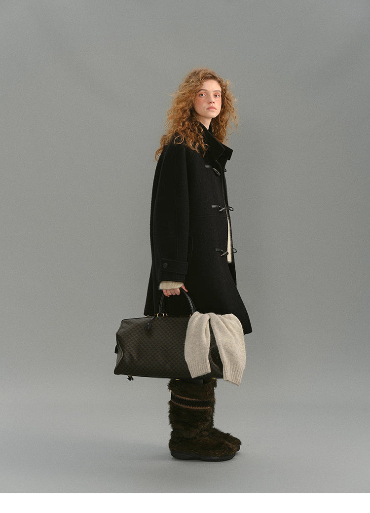 Side full-body view of black toggle coat with travel bag.