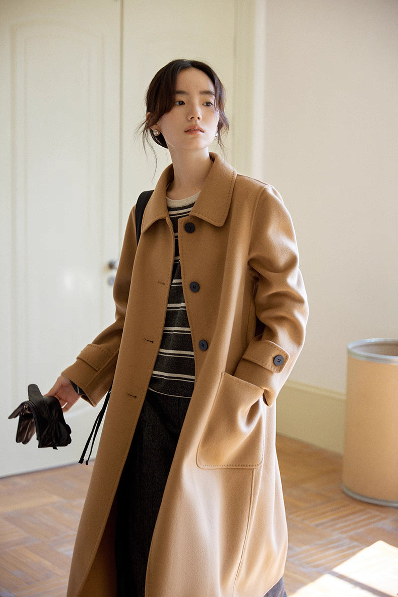Woman wearing an almond-camel cashmere wool long coat, front view, holding leather gloves in a studio room