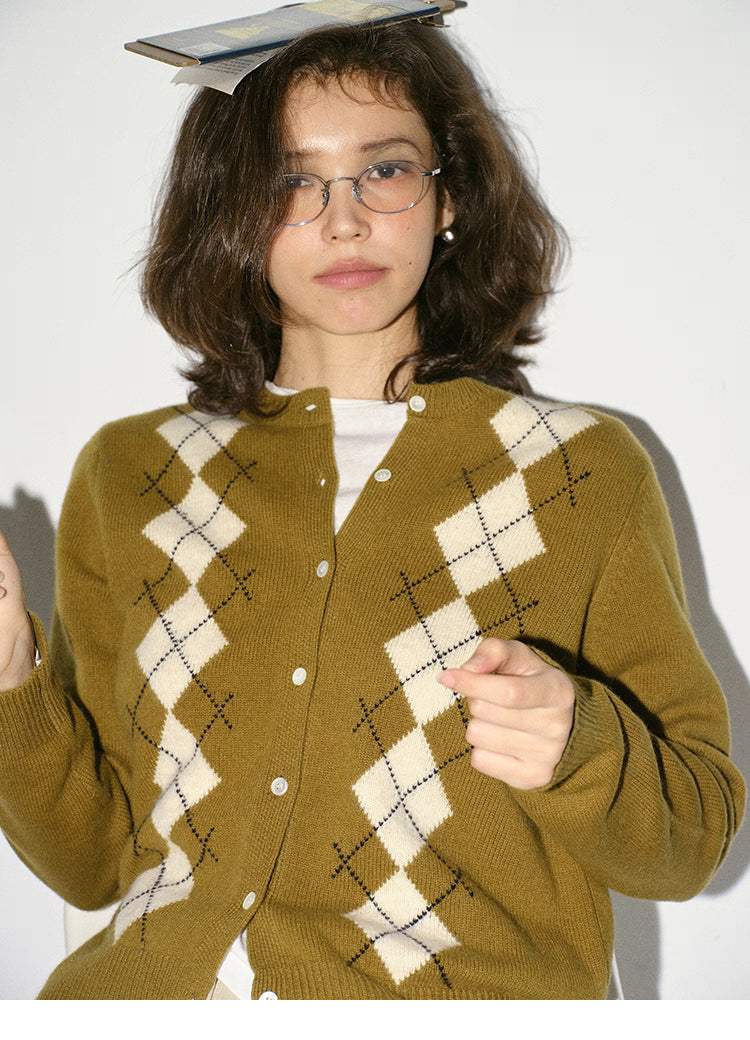 model seated wearing olive argyle cardigan adjusting hair