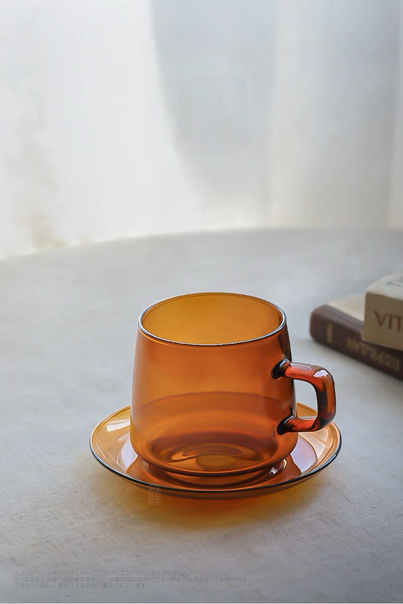Amber Aurora Harmony glass cup and saucer placed in soft natural light setting with books creating cozy lifestyle atmosphere