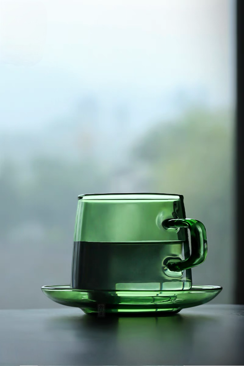 Green Aurora Harmony glass cup and saucer filled with tea in clean minimal setting highlighting transparent glass design