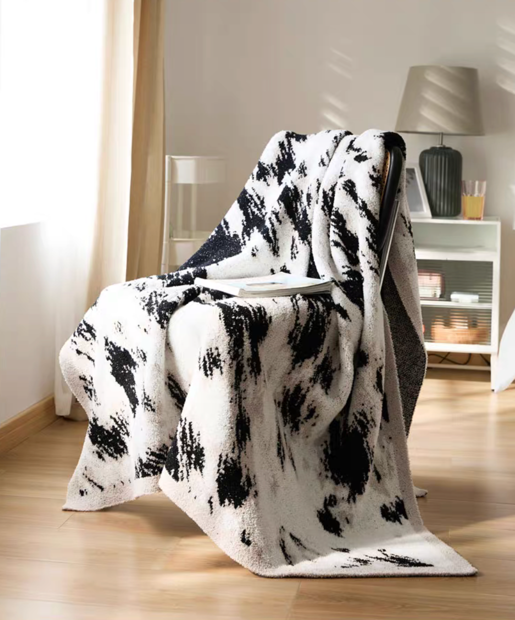 Black and white blanket draped over chair with book on top highlighting relaxed living space and flowing fabric coverage