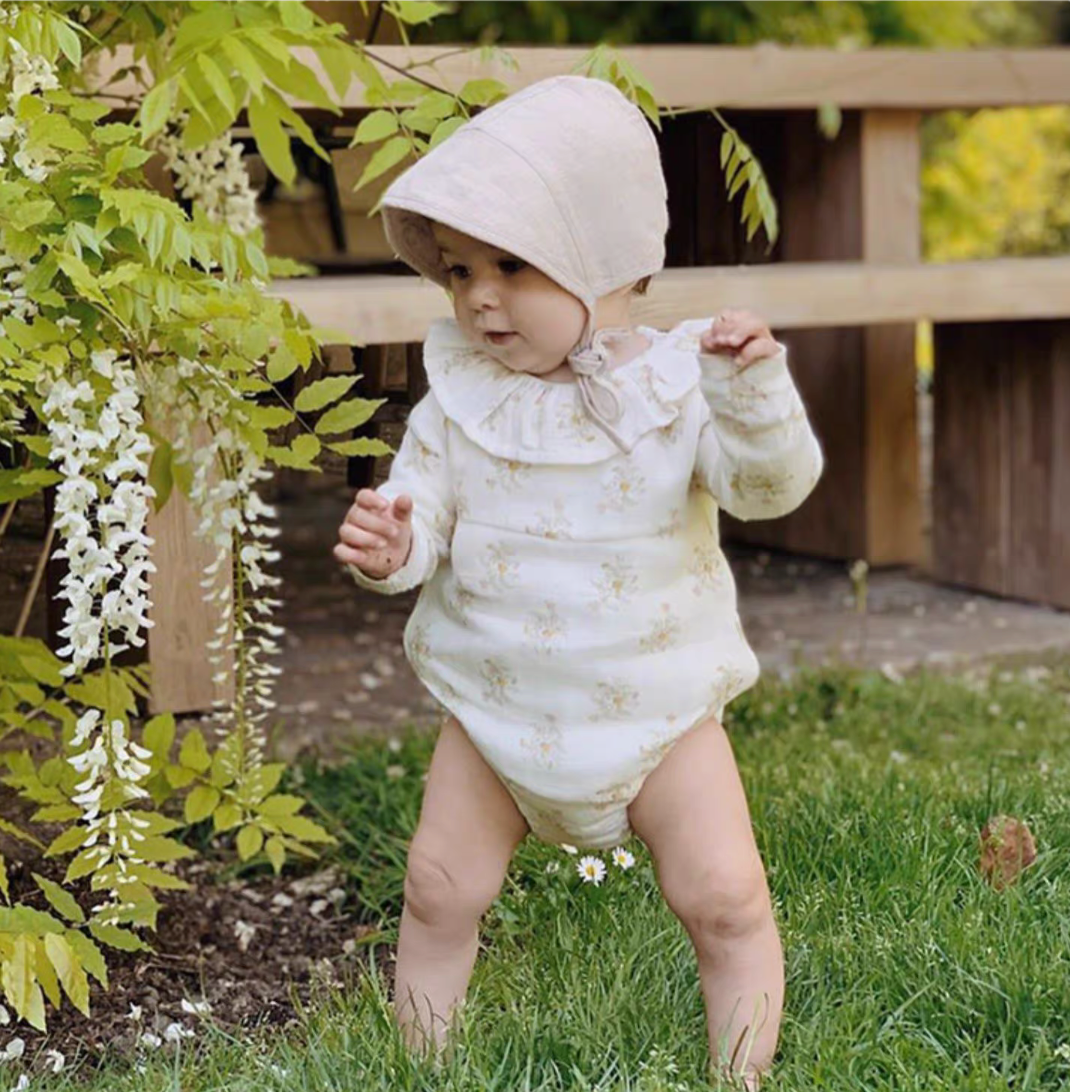 Baby wearing cream linen cotton sun hat walking on grass in garden floral outfit