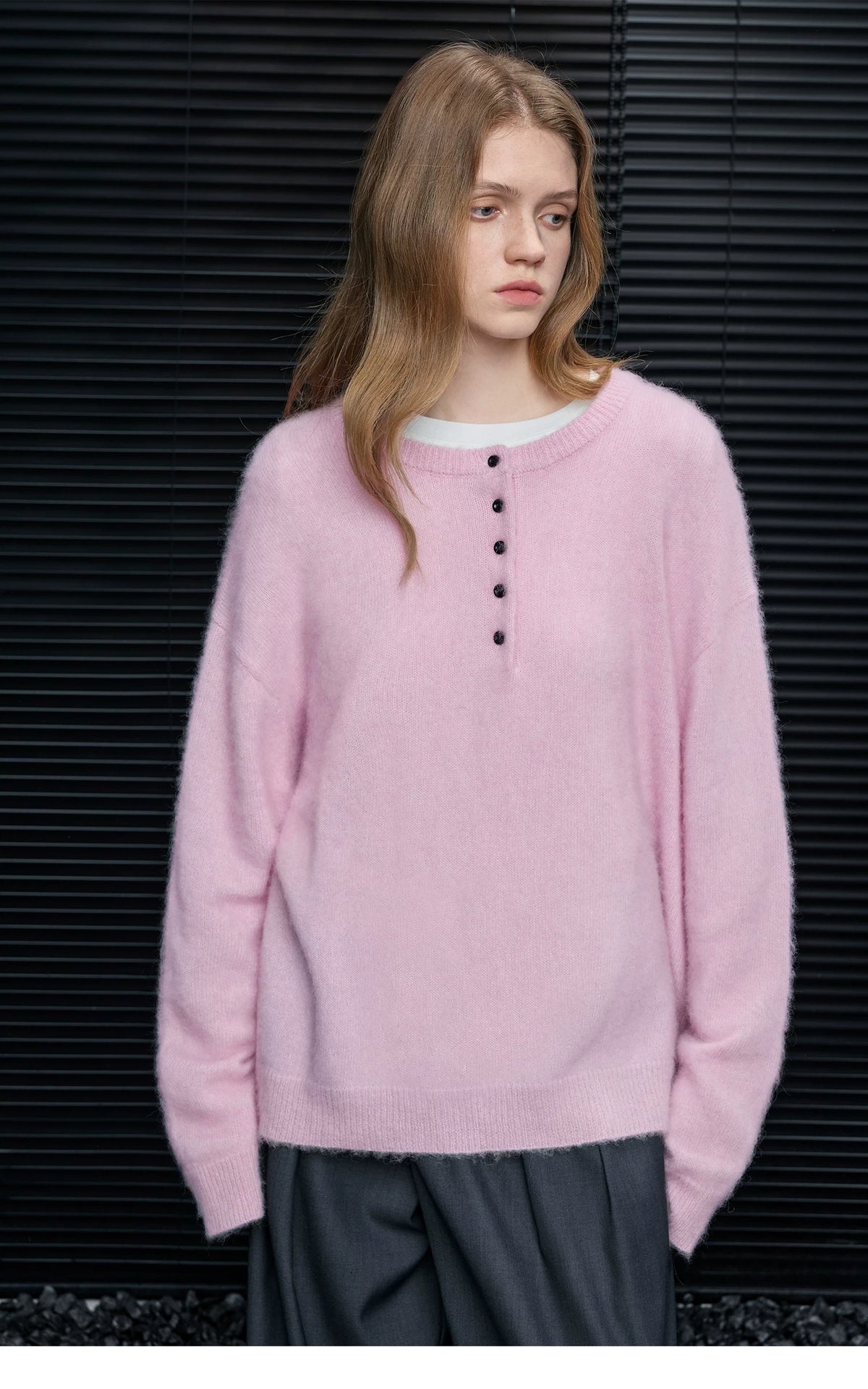 Woman wearing Baby Pink brushed alpaca Henley sweater with black buttons over a white tee and grey trousers