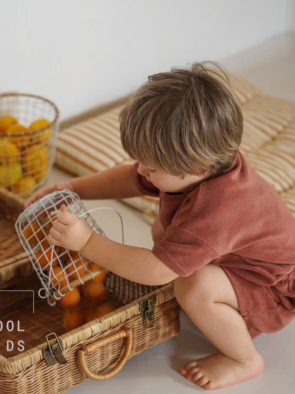 Baby wearing rust red lounge set playing with basket of oranges cozy lifestyle scene