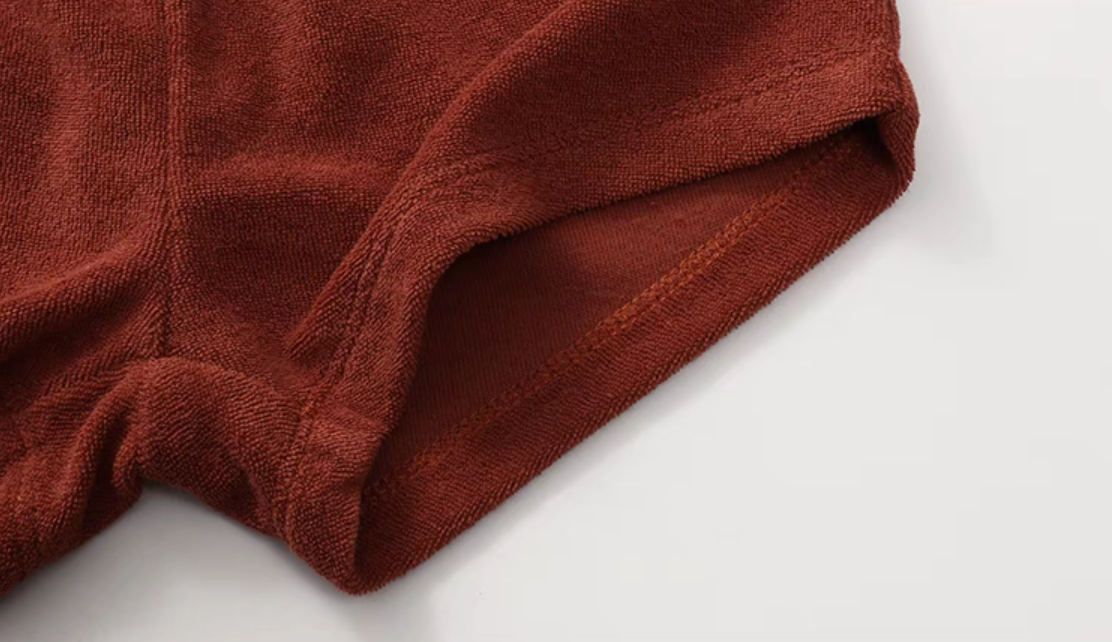 Close-up of rust red baby shorts hem stitching showing soft breathable cotton texture