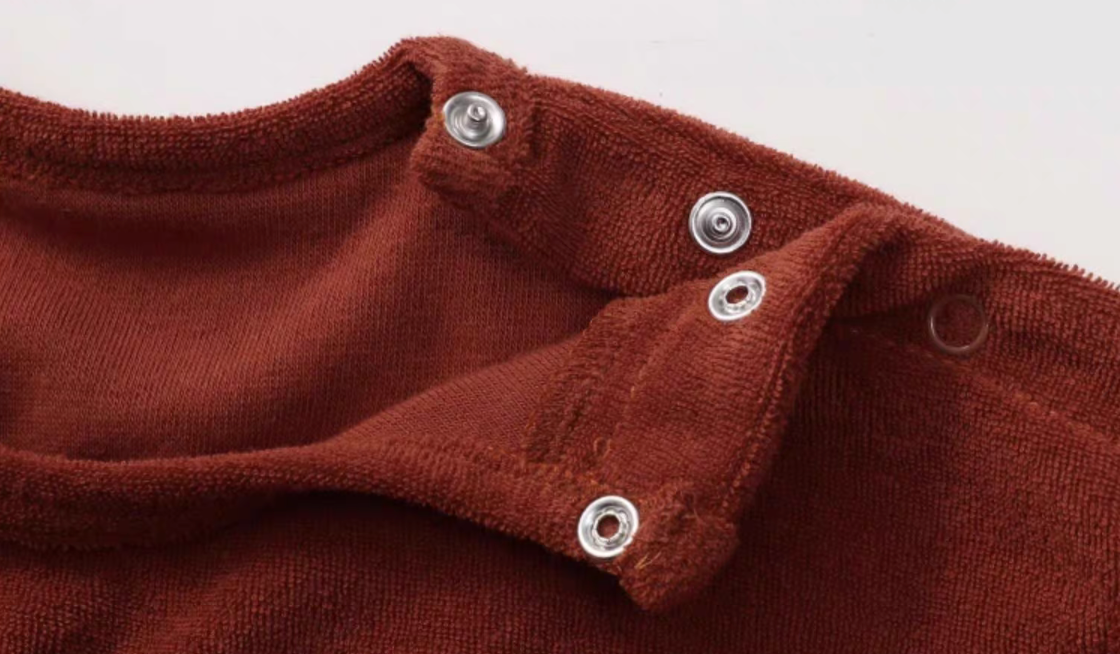 Close-up of rust red baby top shoulder snap buttons showing easy dressing detail