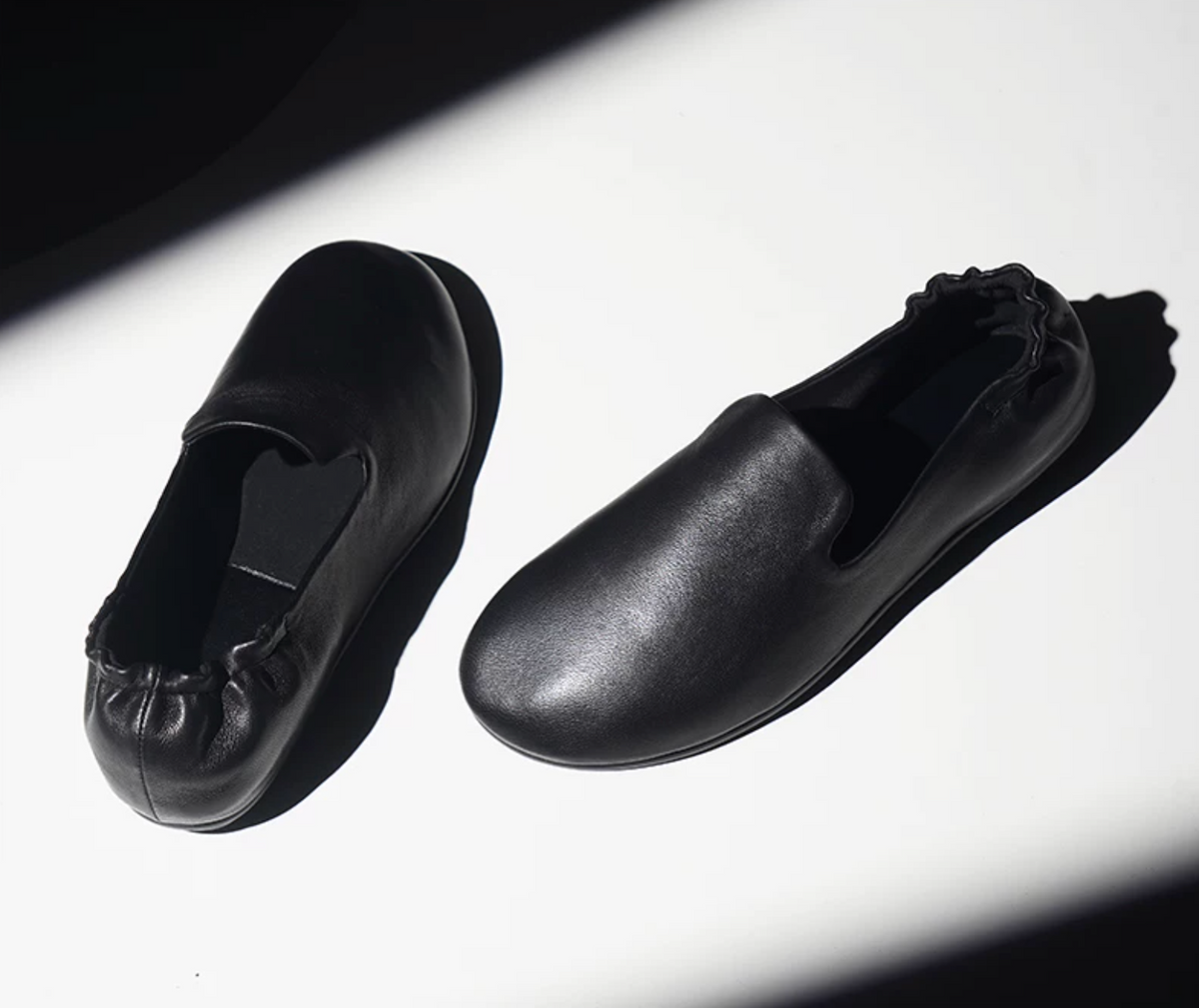 Pair of Black lambskin slipper loafers with gathered elastic heels, angled view in dramatic light