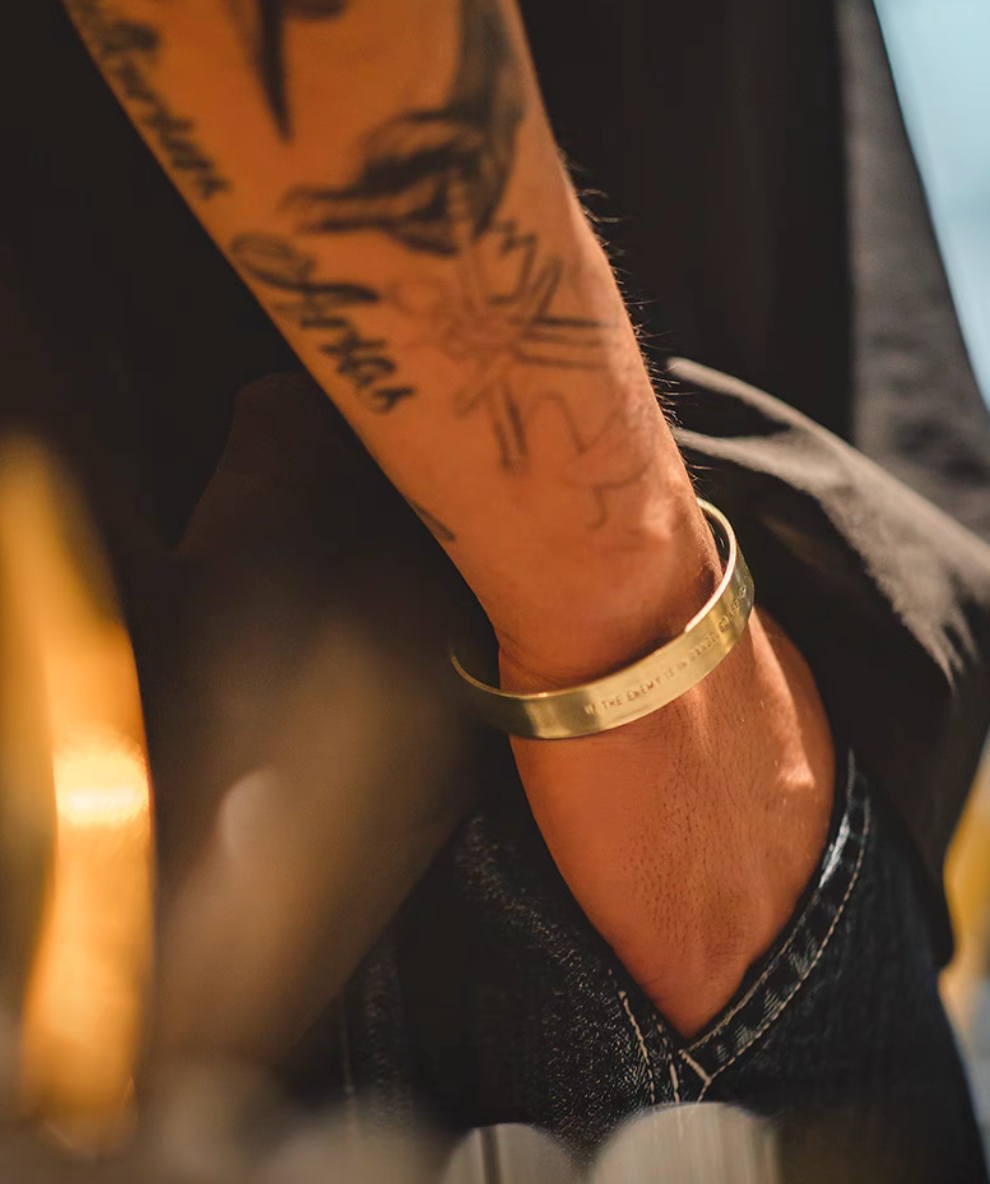Person wearing brass cuff bracelet on wrist showing engraved message in natural color finish