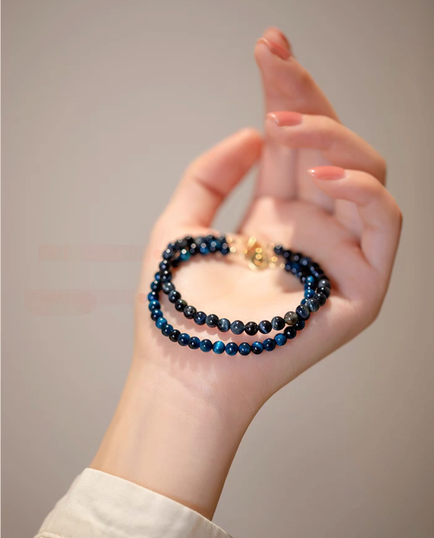 Two Blue Tiger’s Eye bracelets with natural blue beads held in hand showing double strand styling and gold clasp detail