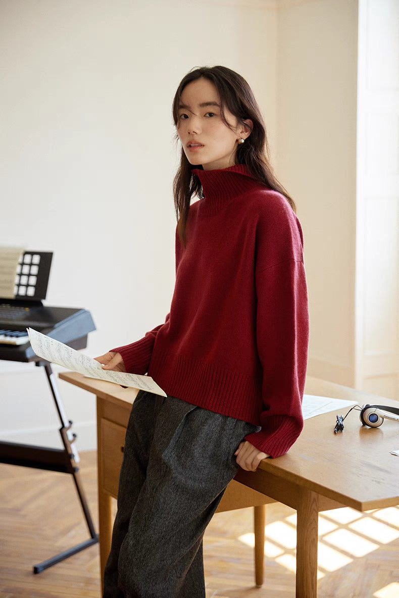 Model in red wool-cashmere turtleneck sweater leaning against desk showing relaxed fit, dropped shoulders, and soft knit finish