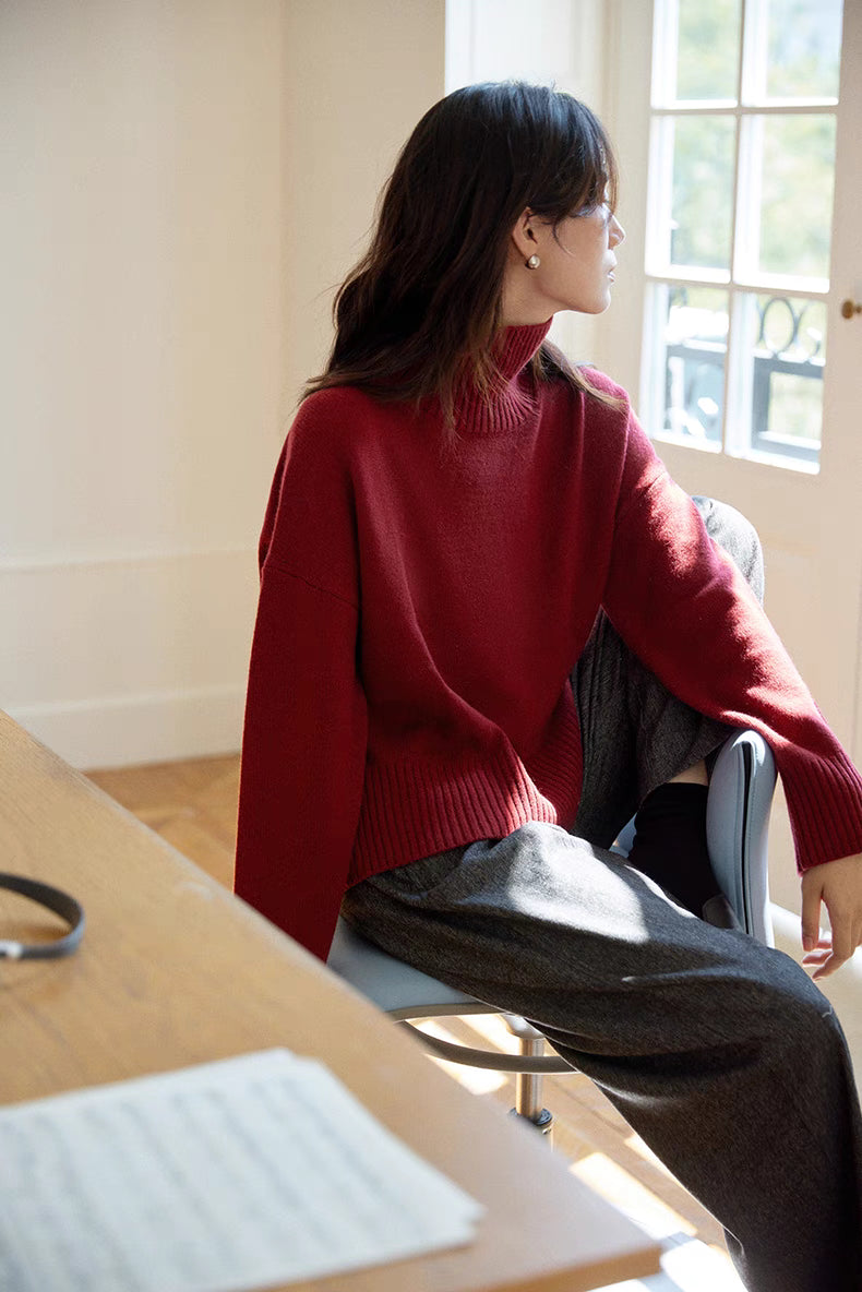 Model in red wool-cashmere turtleneck sweater sitting by window looking outside highlighting soft texture and relaxed winter styling