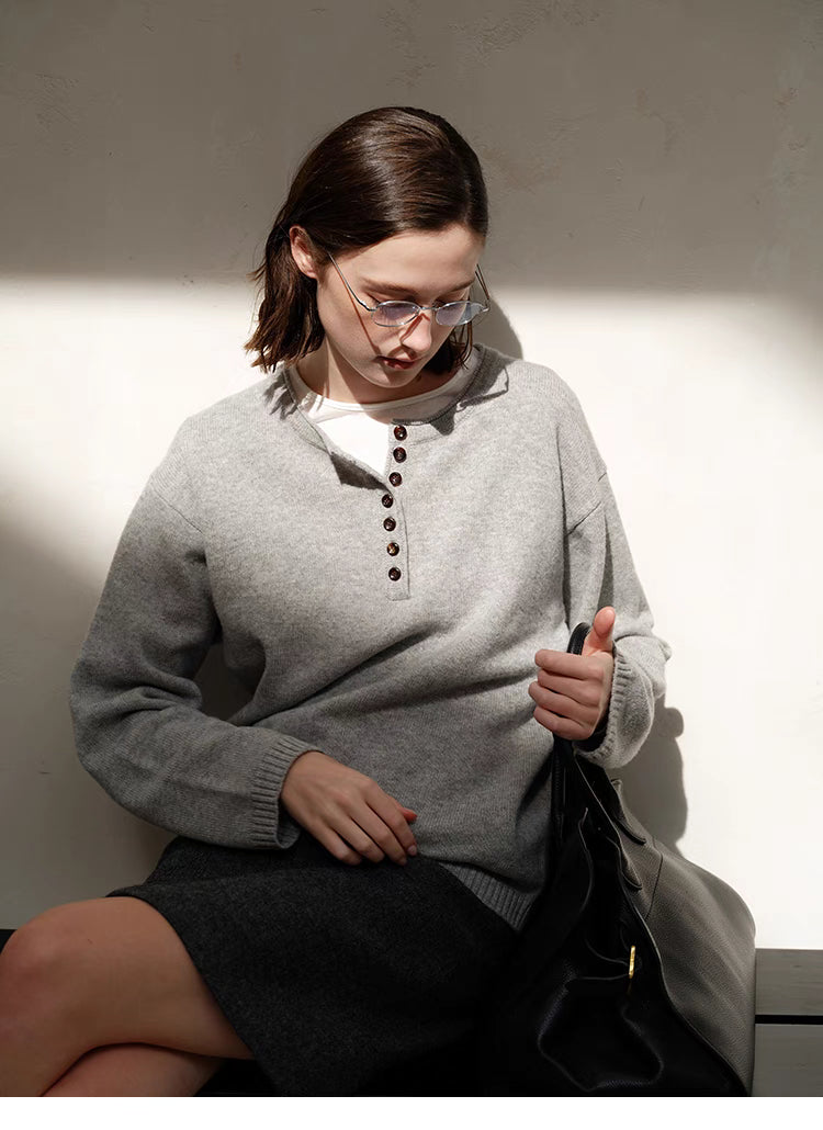 Model wearing light gray Buttoned Henley Knit Pullover Sweater with half-button placket, seated front view