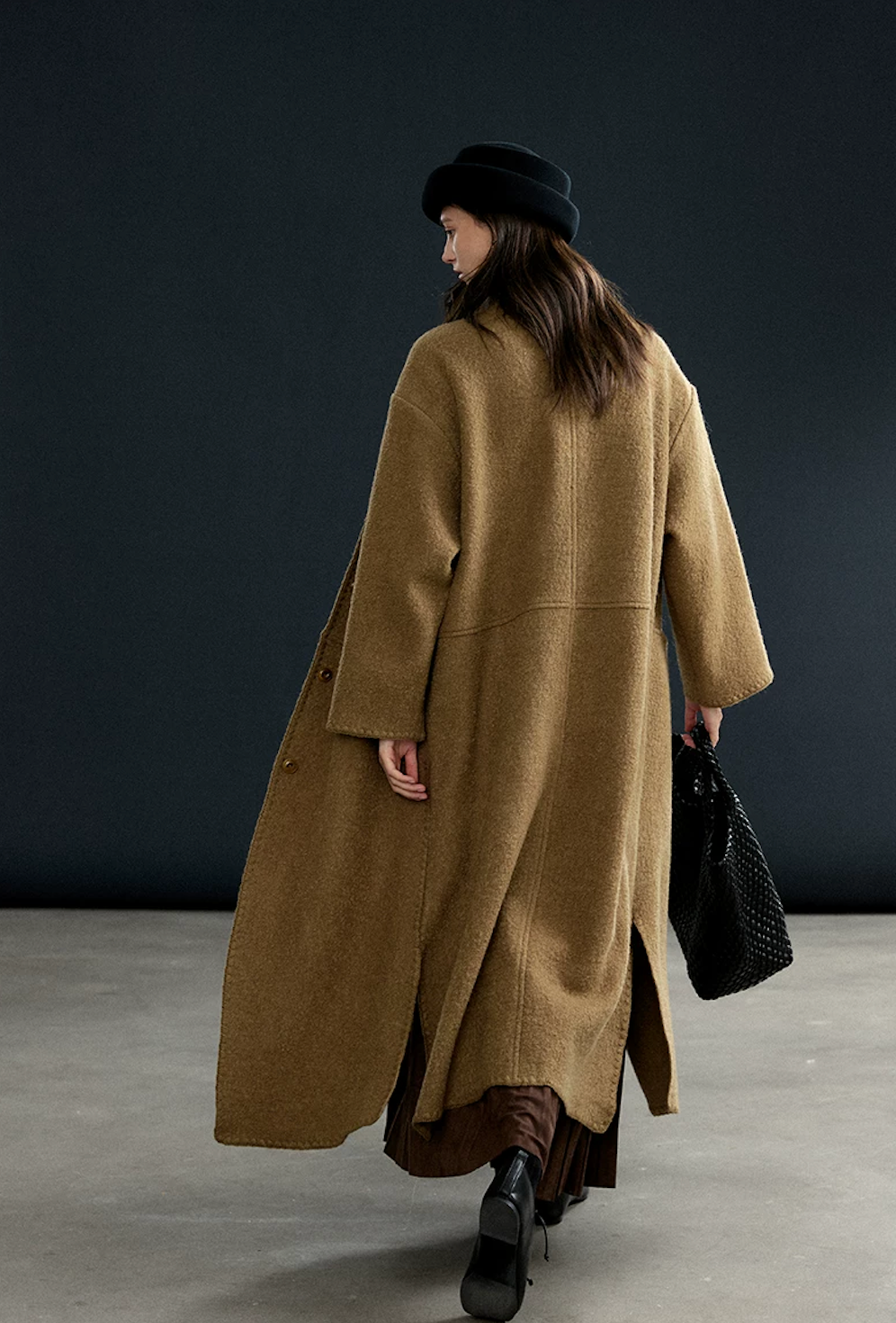Back view of a Camel long wool coat showing the yoke seam, side slits, and stitched hem