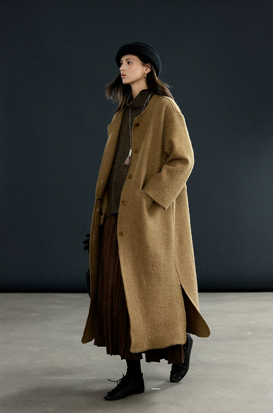 Camel collarless wool coat worn open without the scarf, showing the button front and side pocket