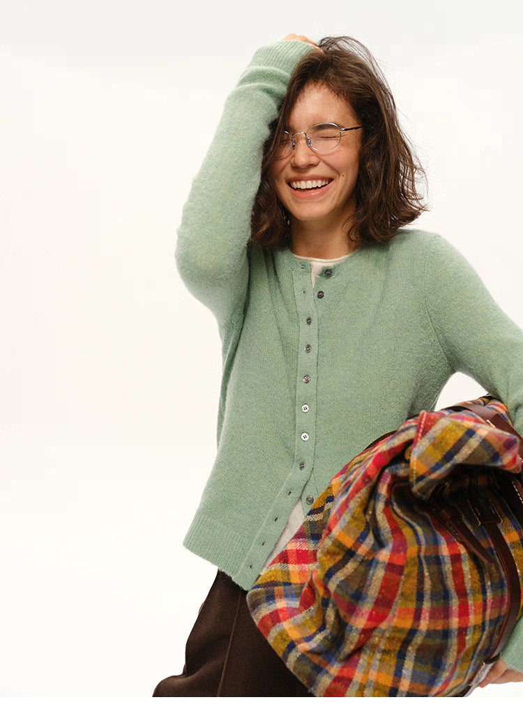 Woman smiling in mint green alpaca cardigan holding colorful plaid blanket bag
