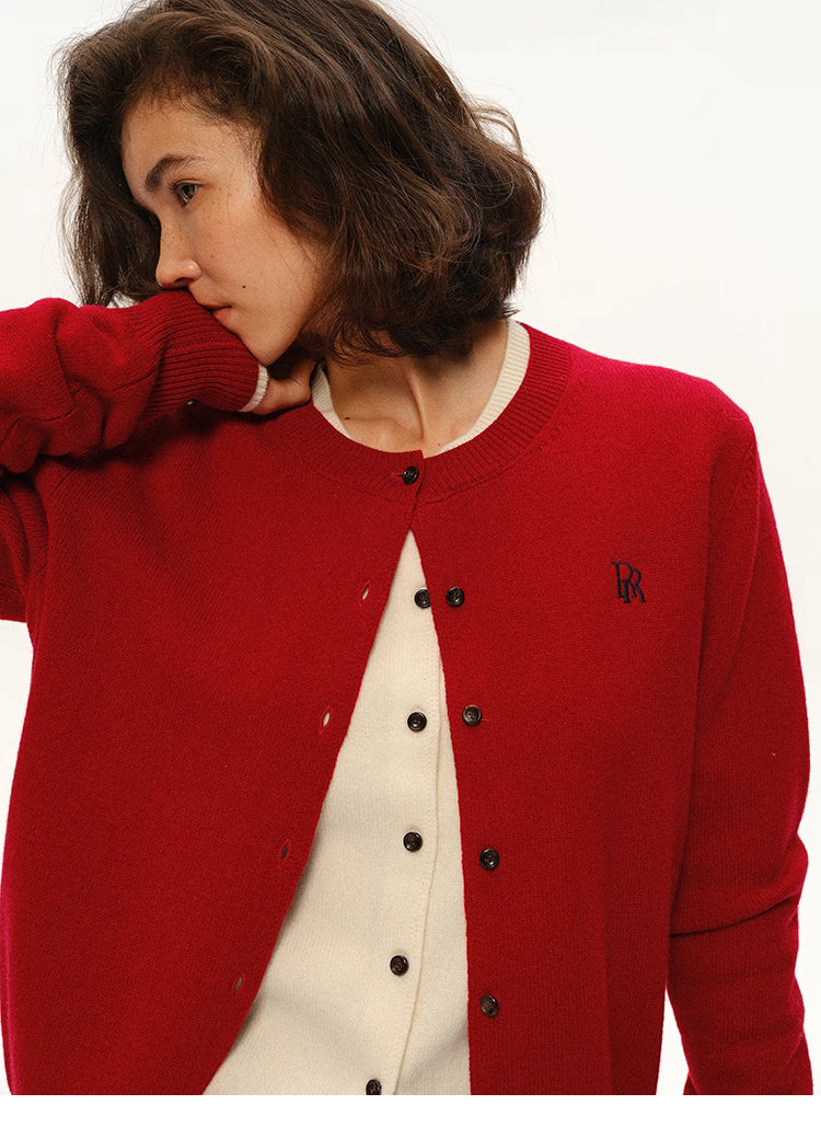 Close-up of cherry red wool cardigan showing embroidered logo and layered cream knit underneath