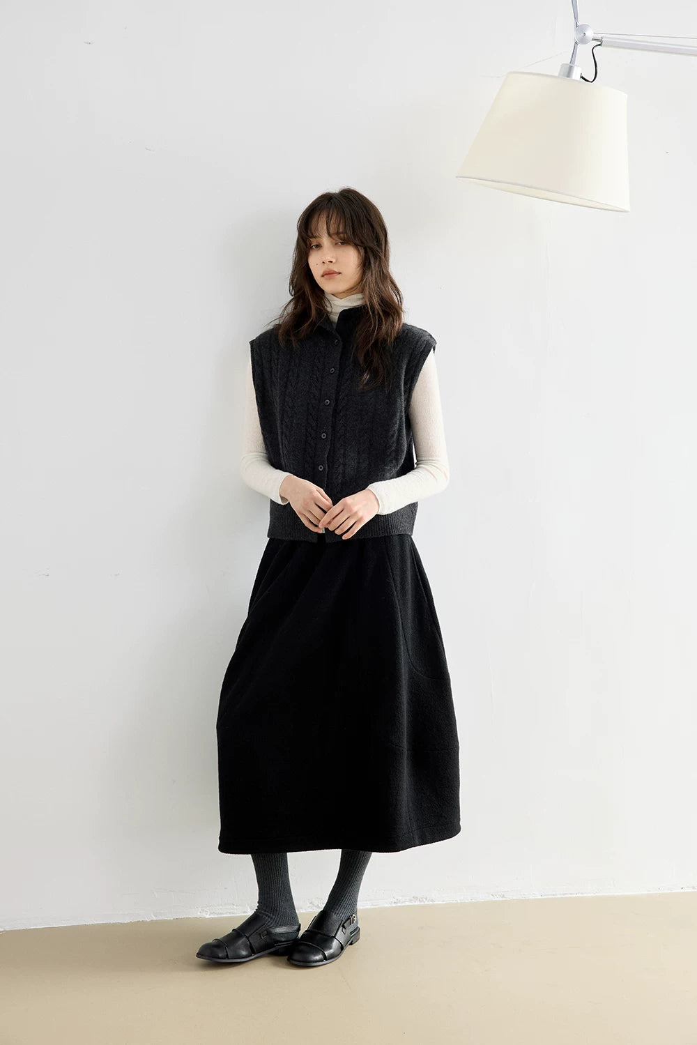 Full-length view of woman in Charcoal Gray cable knit wool vest over an ivory turtleneck with a black midi skirt