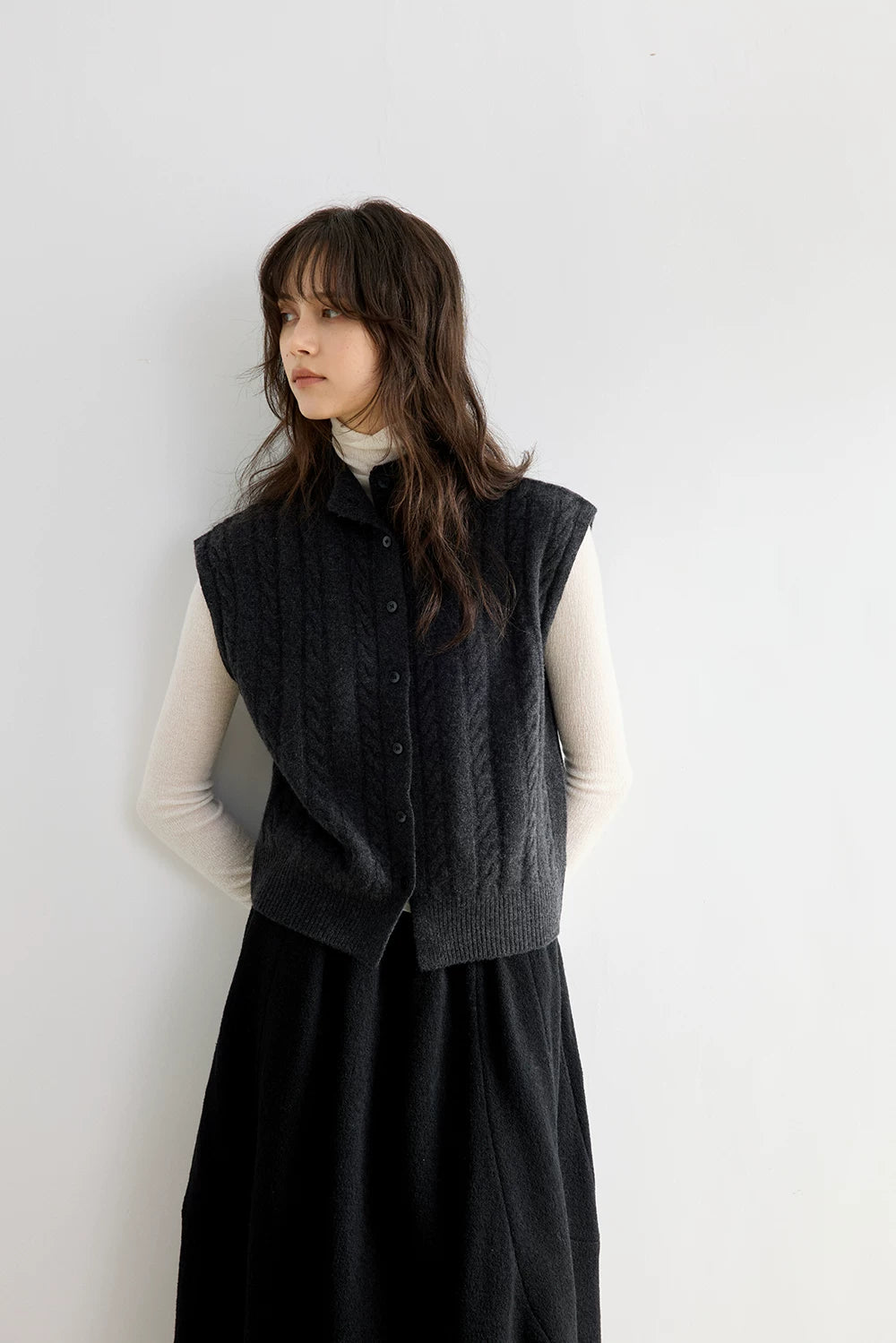 Charcoal Gray sleeveless cable knit vest layered over an ivory turtleneck, three-quarter front view