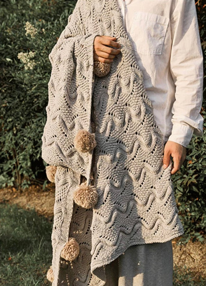 Gray chenille throw blanket wrapped around person outdoors showing soft knit texture and pom pom detail