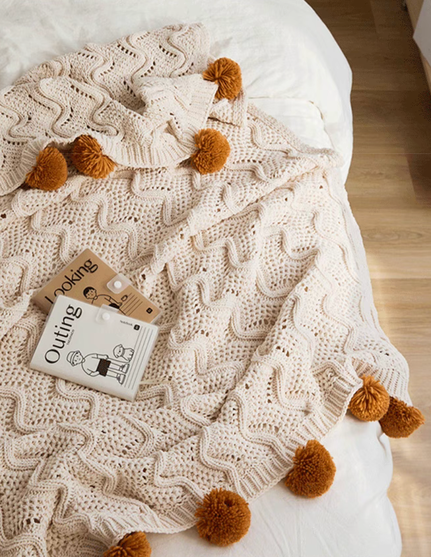 Close-up of white chenille throw blanket showing soft knit texture with pom pom tassels and cozy details