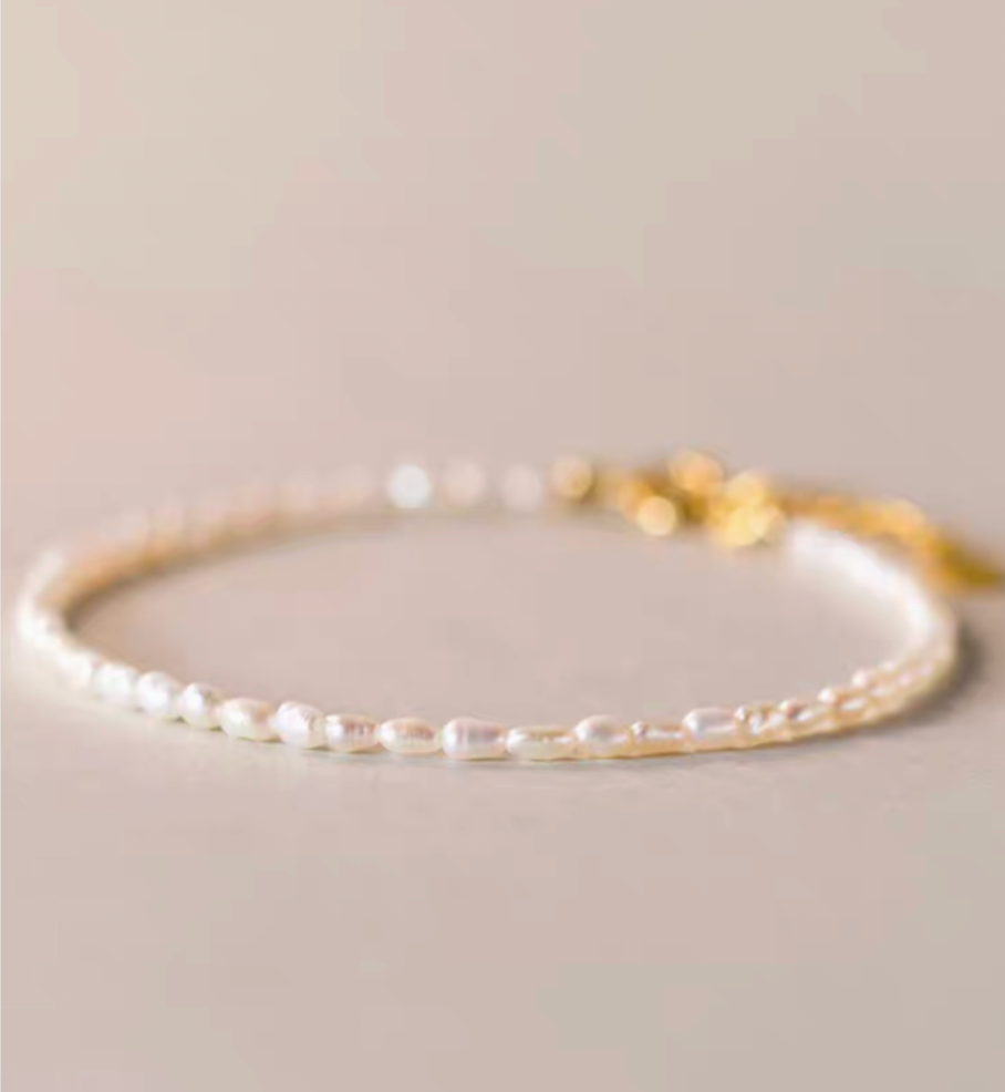 Minimal flat lay close-up showing classic pearl bracelet in natural color with delicate small pearls and gold clasp detail