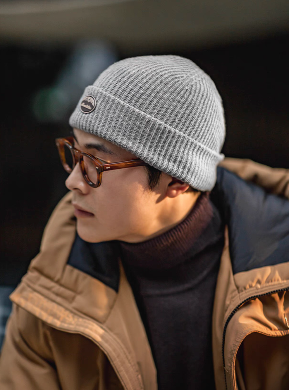 Model wearing Classic Ribbed Knit Beanie with Logo Detail in gray styled with glasses and winter jacket for an urban casual look