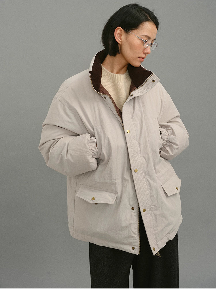 Model wearing a light greige down coat with a visible brown inner collar, looking sideways.