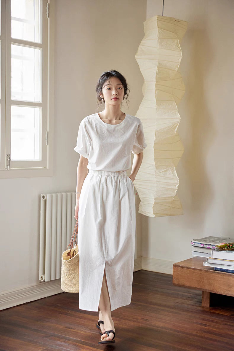 Model wearing Coastal Breeze Cotton Top & Skirt Set in white walking forward featuring breathable cotton fabric and elegant summer midi skirt design