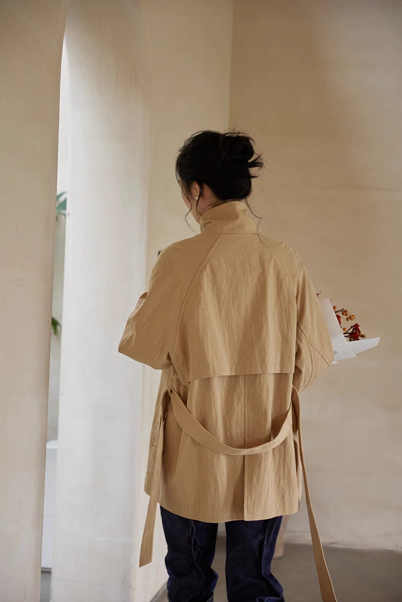 Back view of light brown short trench coat with belt hanging loose and back flap detail